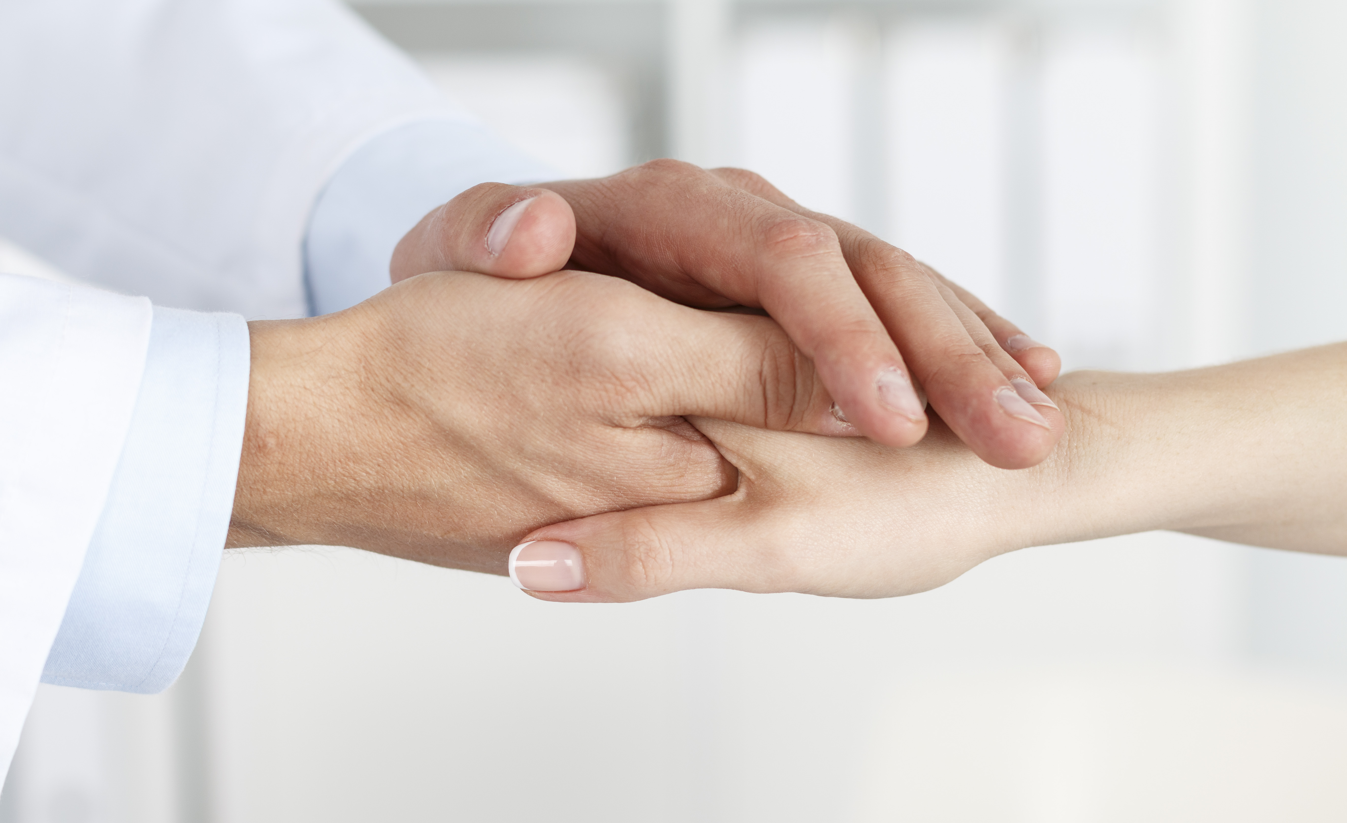 Friendly male doctor's hands holding female patient's hand